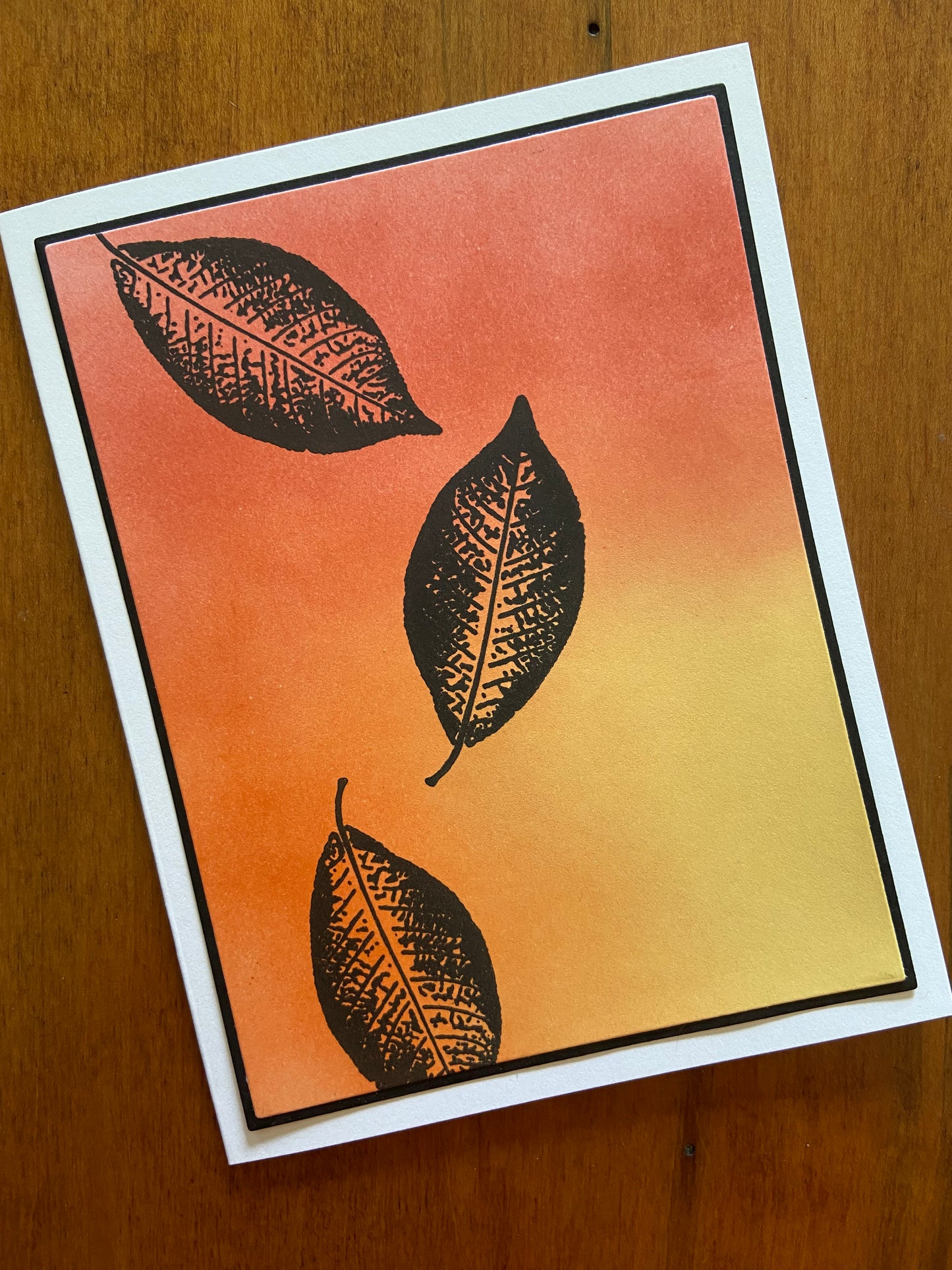 Autumnal oranges, yellows, and reds are ink blended together. 3 Black silhouette leaves are stamped here and there.