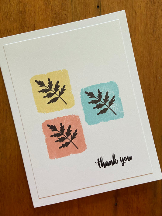 Thank you handmade card. Yellow, coral pink, and turquoise squares stamped in a group of 3 and then each block is stamped with black ferns. A simple thank you is stamped in black in the bottom right corner.