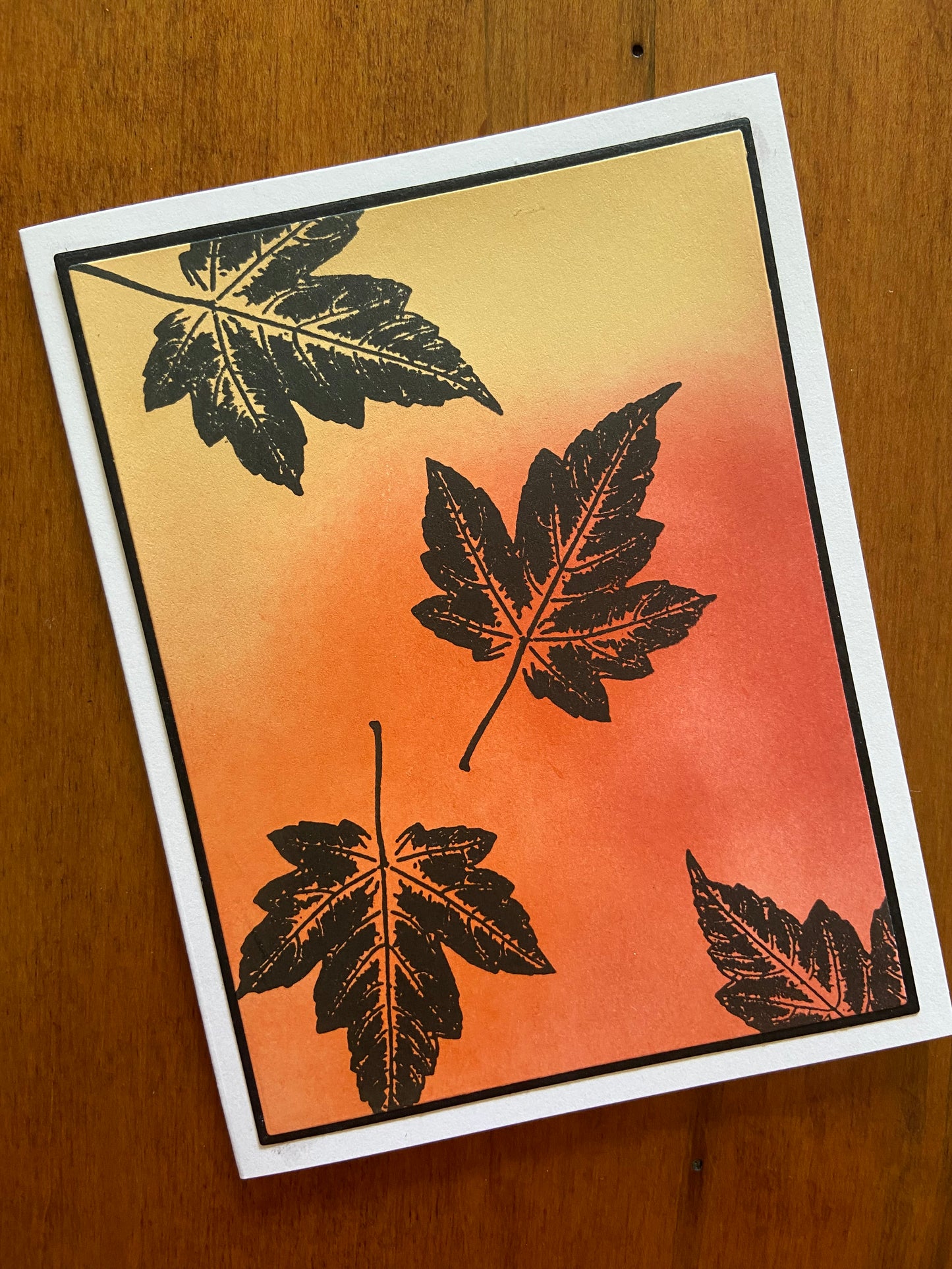 Autumnal oranges, yellows, and reds are ink blended together. 4 Black silhouette maple leaves are stamped here and there.