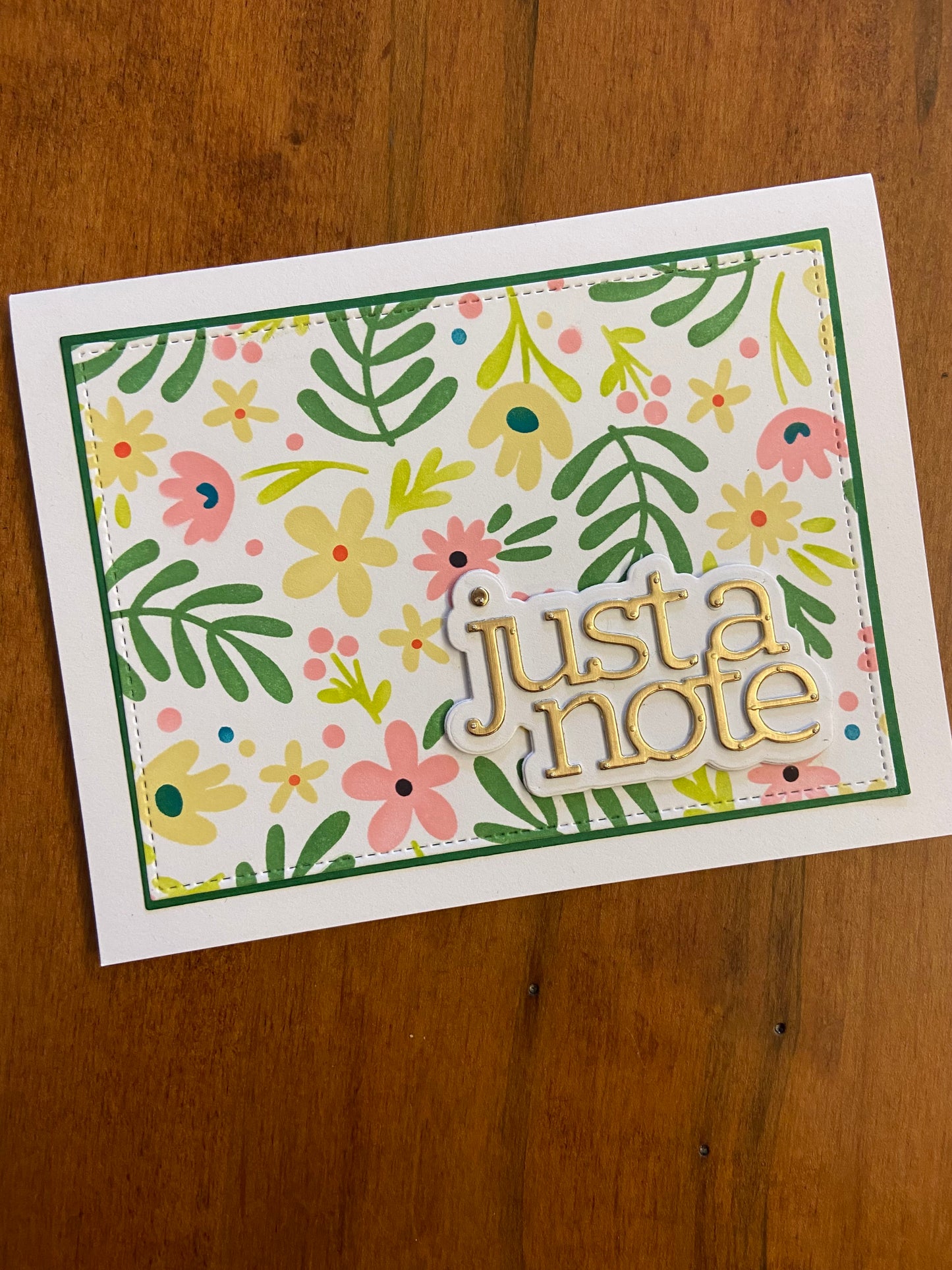 Dainty flowers and foliage just a note hand made card. Featured colours of yellow, coral pink, and green. A gold metallic just a note die cut in bottom right corner finishes the card.