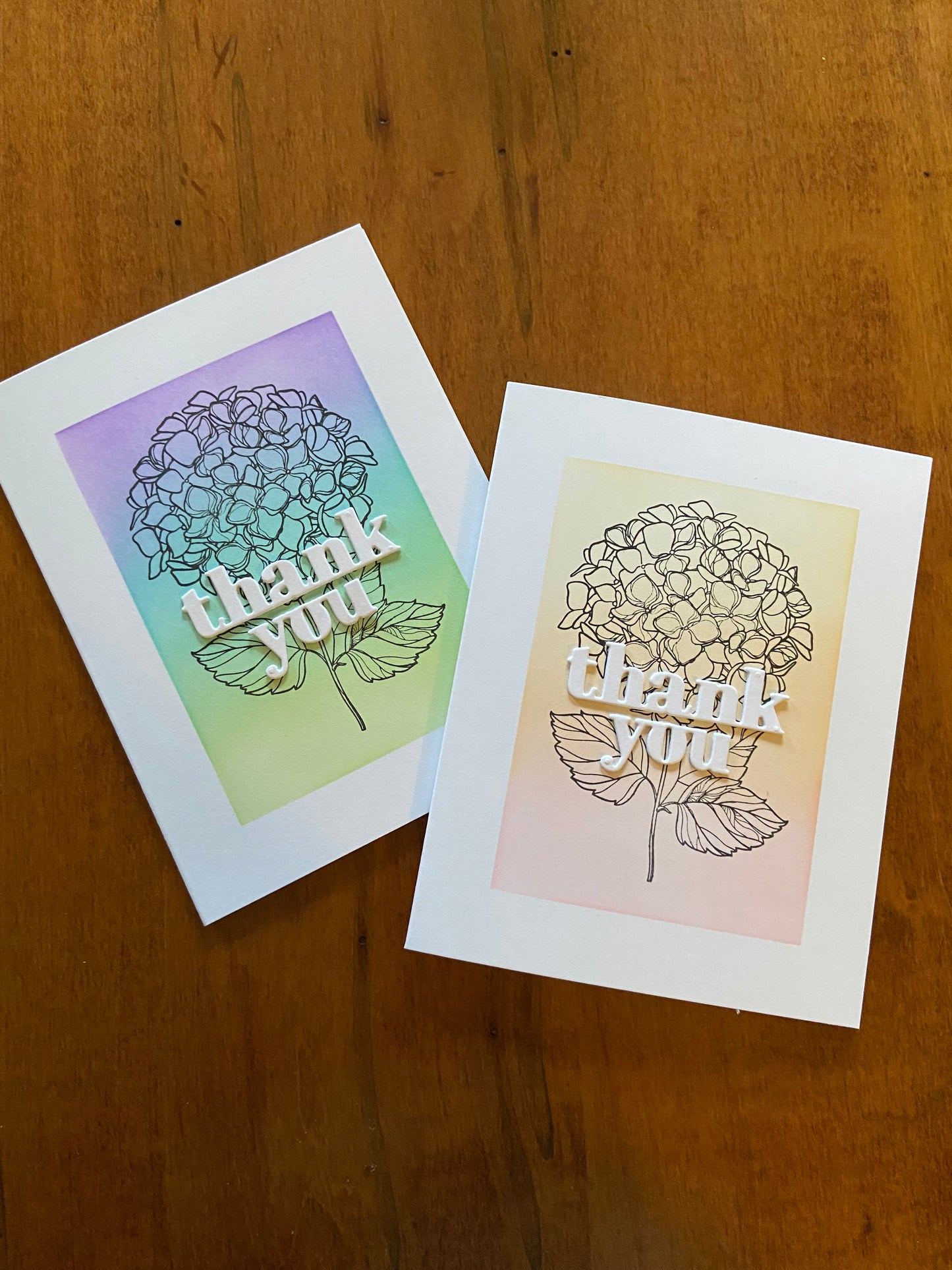 Thank you handmade cards. Ink blended backgrounds with a hydrangea cluster outline stamps for the focal images. Bold white thank you die cut sentiments are placed on top.
