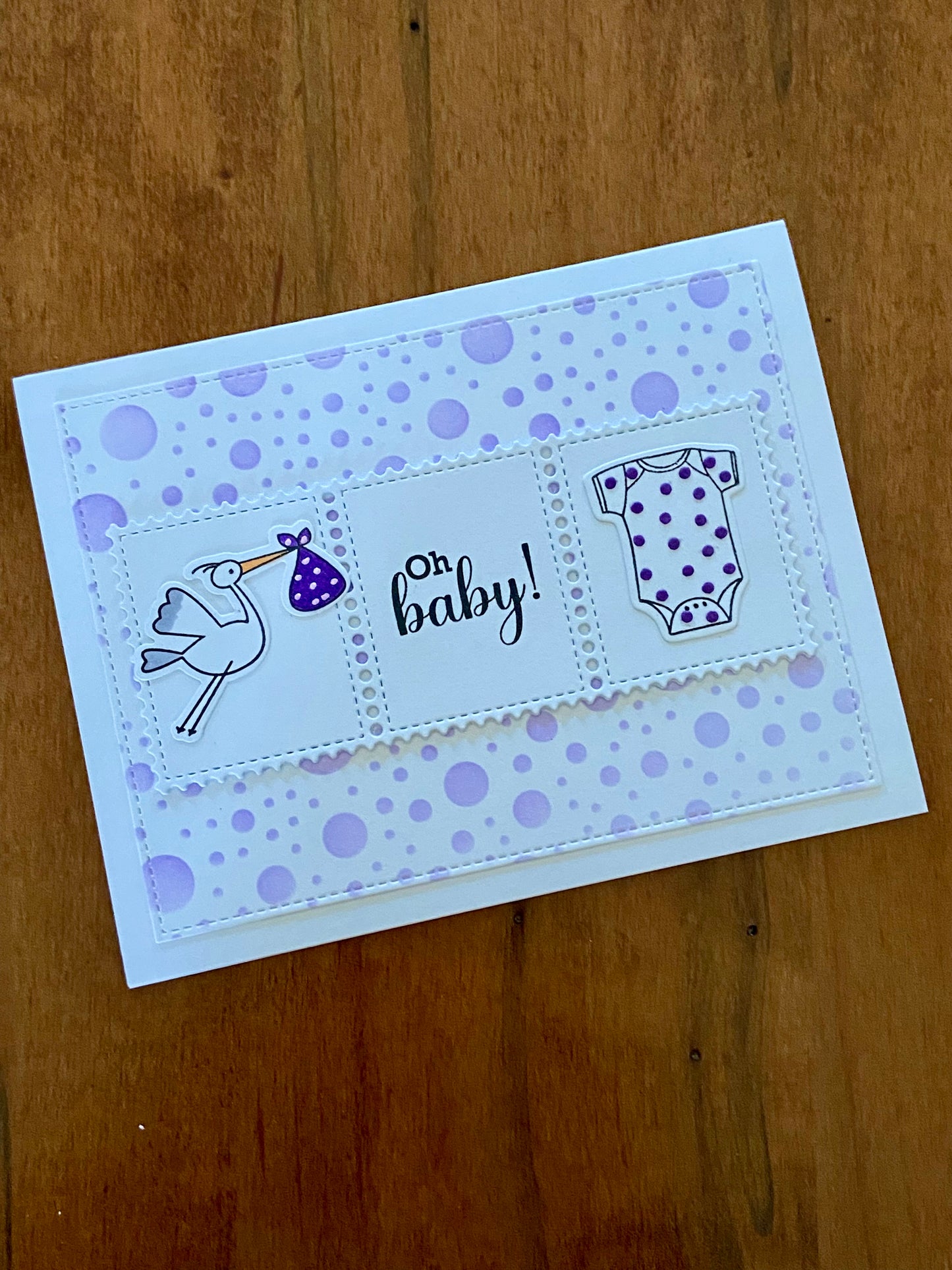 Oh Baby Shower card. Purple polka dot background. A rectangular centre panel with a stork carrying a purple bundle and white onsie with tiny purple dots and the sentiment Oh Baby in between.
