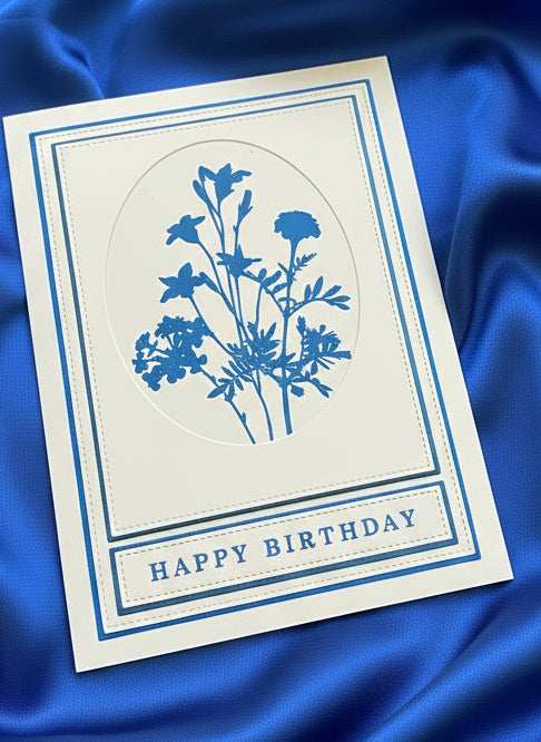 Greeting card with blue floral design and 'Happy Birthday' text laid on a blue satin background