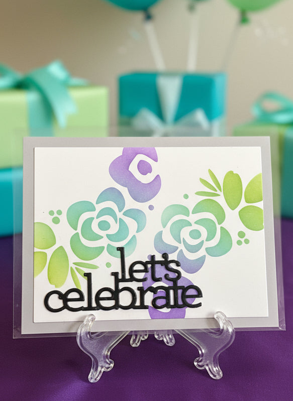 Card with floral design and 'Let's celebrate' text on a purple surface with gift boxes in the background.