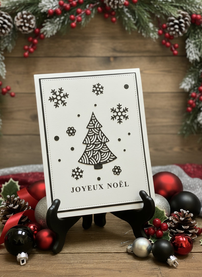 French Christmas card with black ornate tree and snowflakes with 'Joyeux Noël' greeting displayed with festive holiday decorations