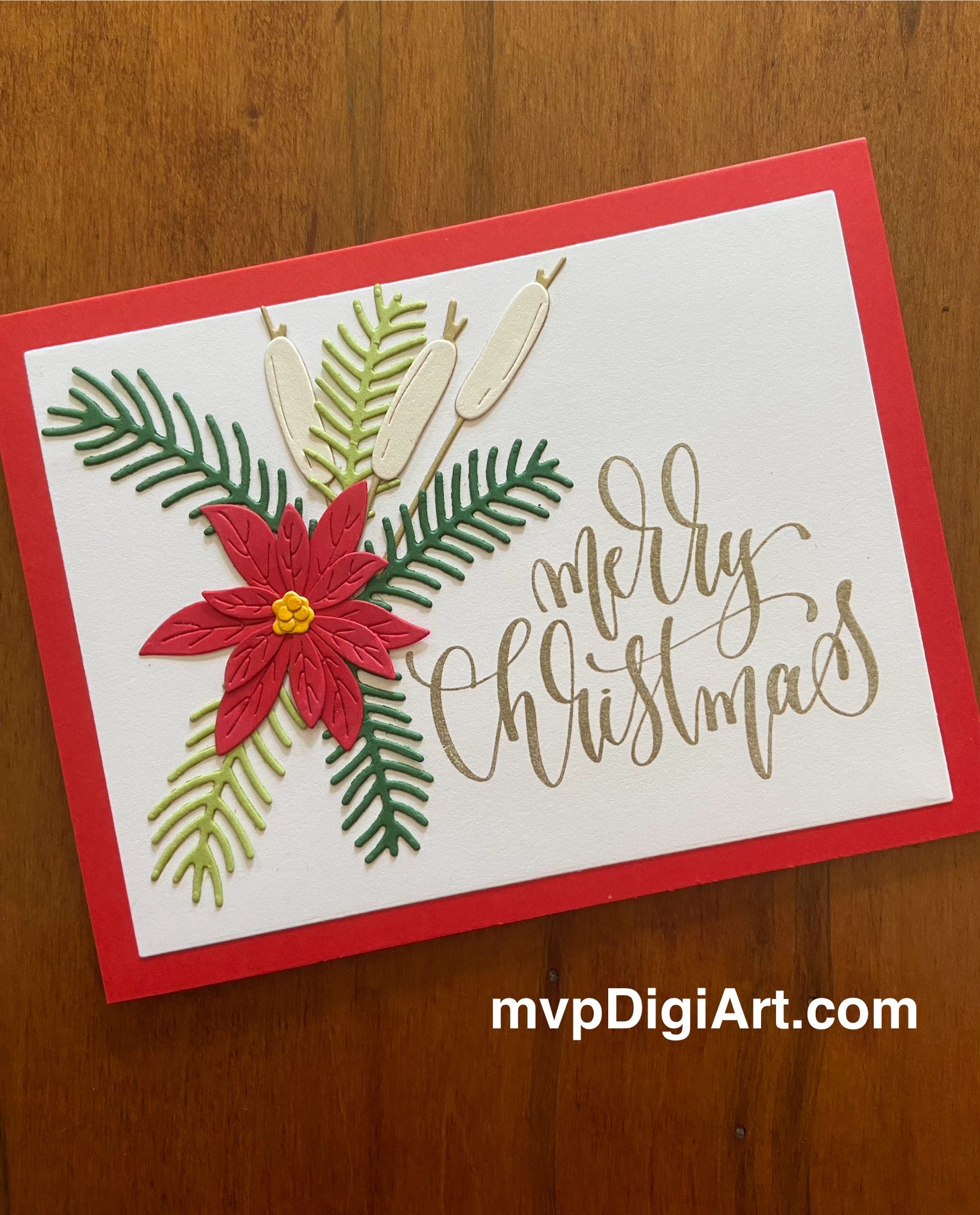 Handmade Christmas card with red poinsettia, spruce sprigs, and cattails on white background atop a red notecard with gold 'Merry Christmas' text
