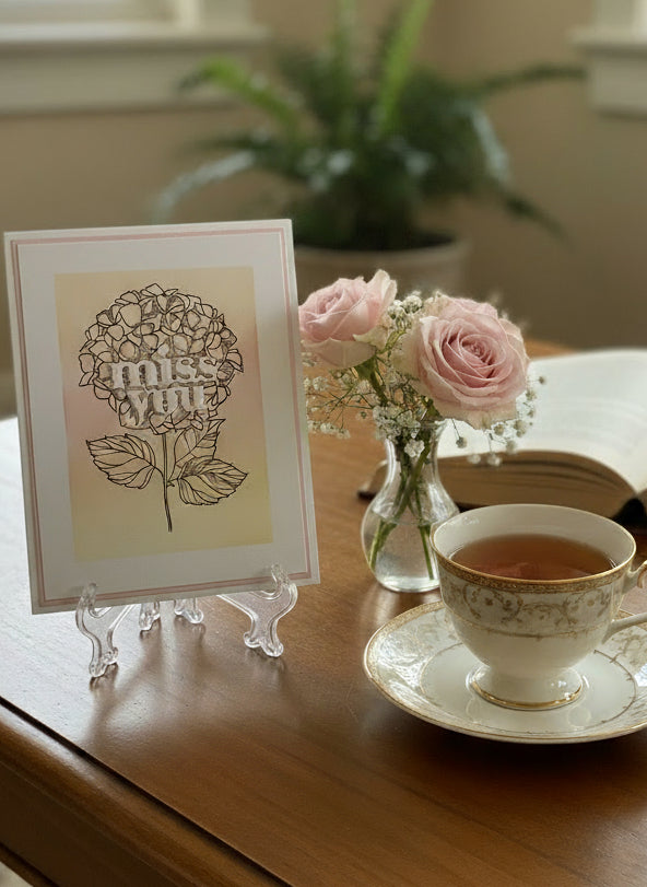 Miss you card with pink and yellow hydrangeas displayed on a table with decorative elements