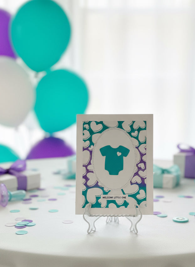 Baby shower card with dark turquoise baby onesie on a floral background, surrounded by gift boxes and balloons.
