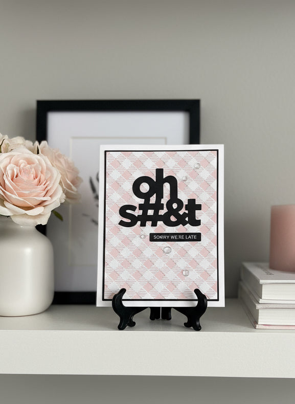 Handmade belated birthday card with pink gingham background and bold 'Oh shit sorry we're late' sentiment displayed on decorated shelf