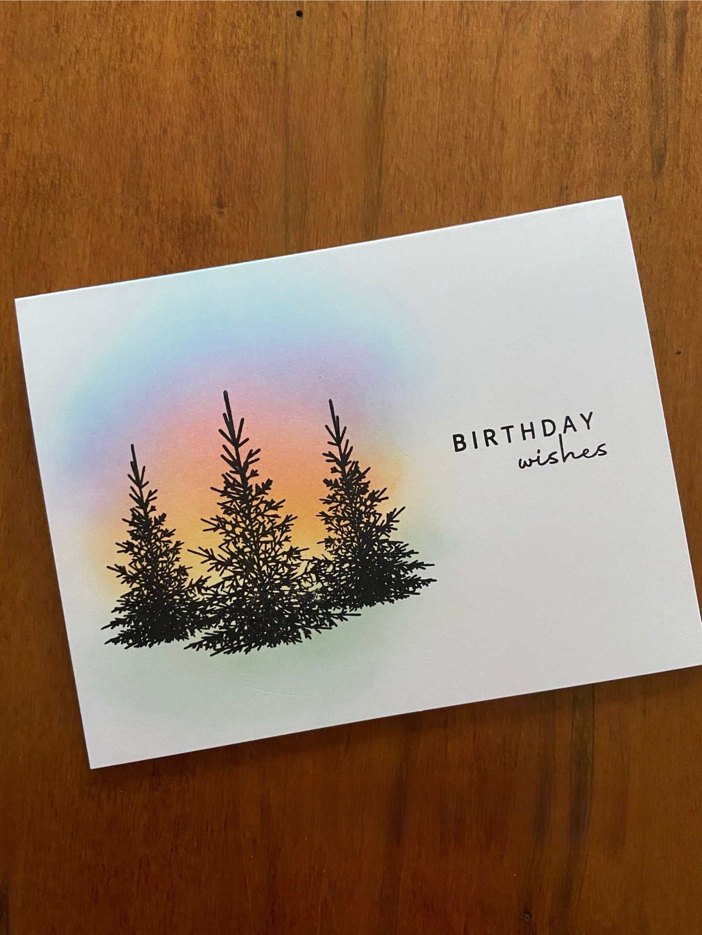 Handmade birthday card featuring a serene sunset sky with warm orange and pink tones and a dark tree silhouette in the foreground