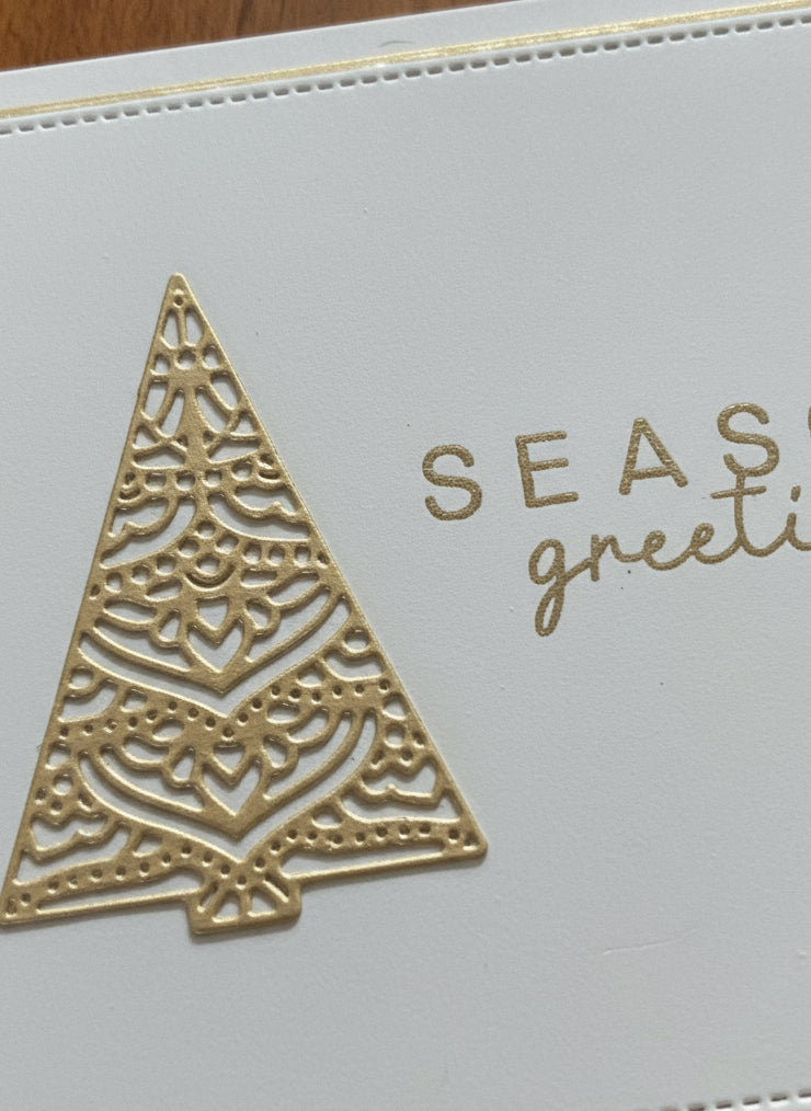Close-up detail of Christmas card showing ornate gold filigree tree on ivory stitched backdrop with heat-embossed sentiment die cut
