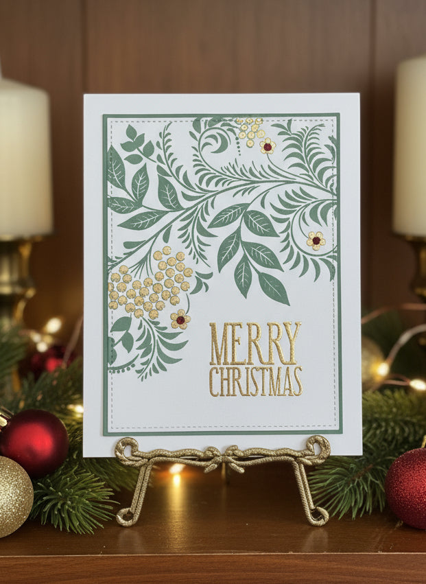 Christmas card with spruce and gold foliage design with gem accents displayed on a decorated shelf with holiday decorations