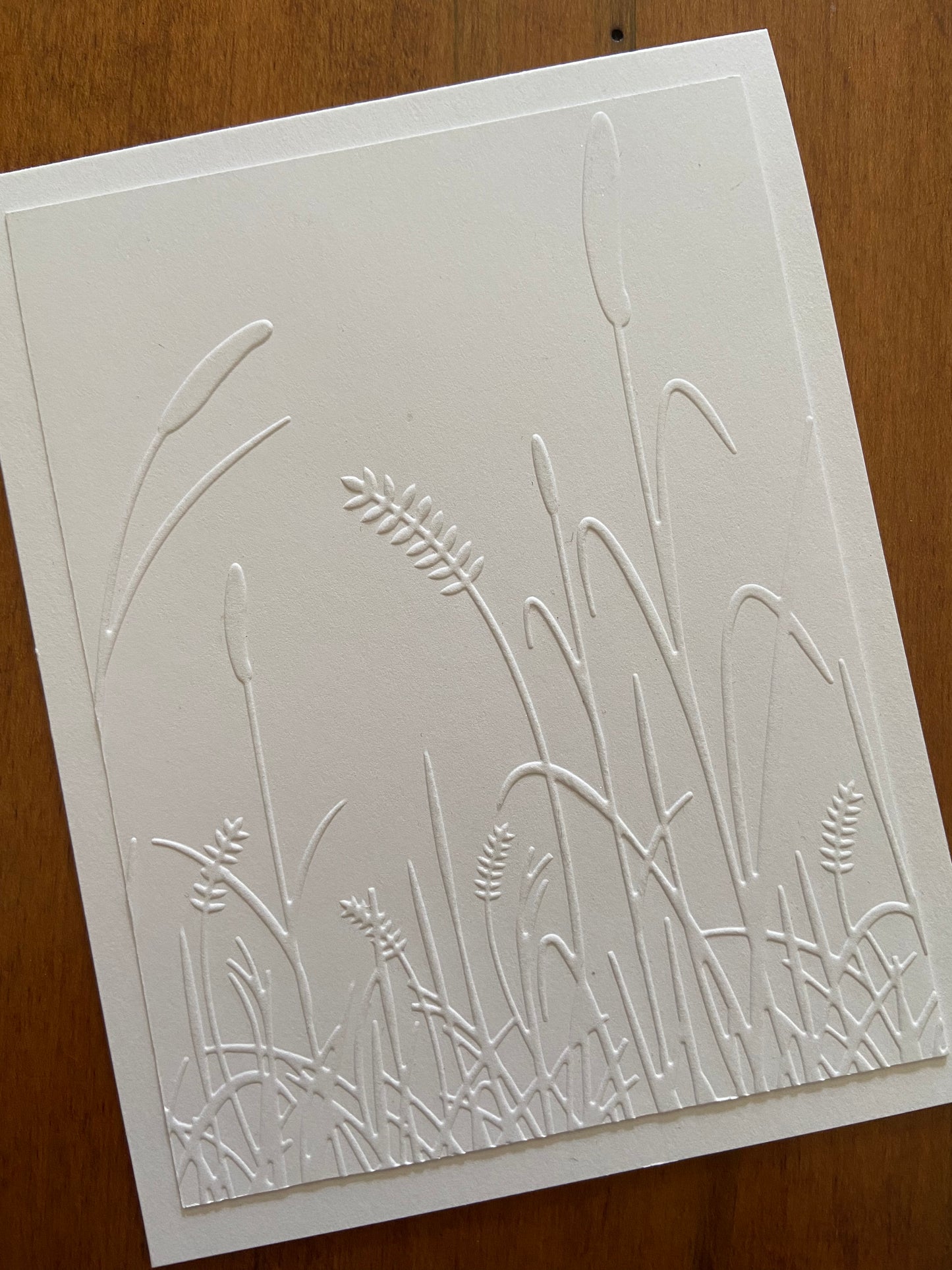 A white panel embossed with cat tails and grasses. A white on white card. A thinking of you sentiment is stamped on the inside.