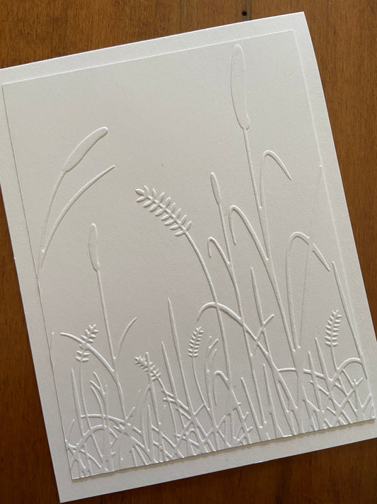 A white panel embossed with cat tails and grasses.  A white on white card. A thinking of you sentiment is stamped on the inside.
