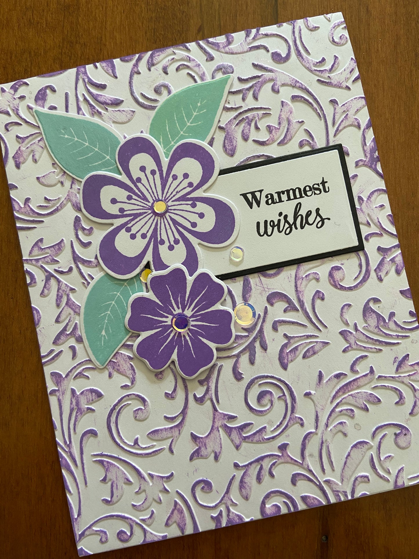 The embossed panel is lightly coloured with purple ink. This card is adorned with some purple flowers and leaf die cuts, a few silver embellishments for sparkle and a “warmest wishes” hand stamped sentiment is tucked in behind the flowers.