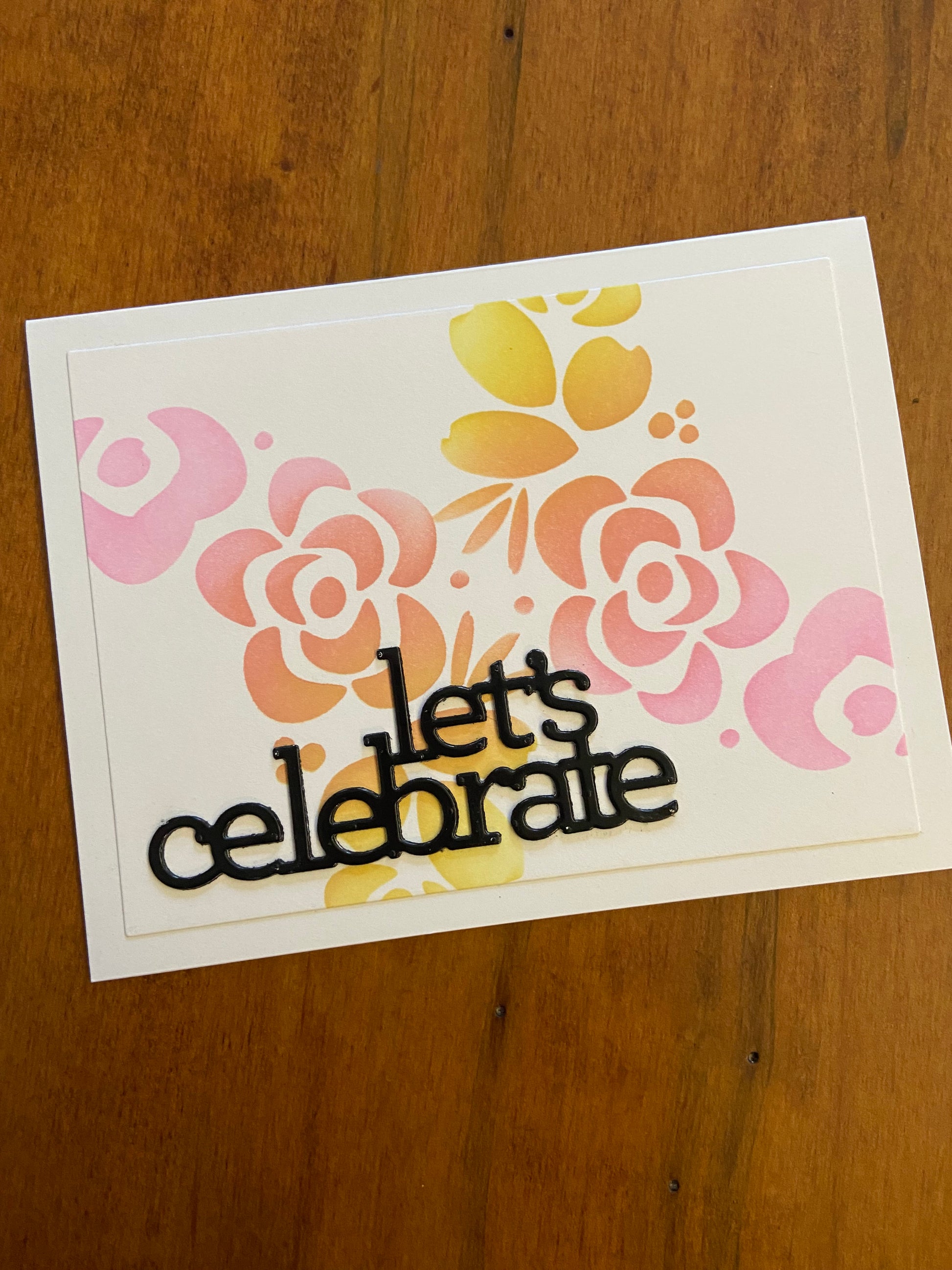 Modern Flowers Let’s Celebrate handmade card. Ink blended modern flowers stencil in shades of pink, orange and yellow. A lets celebrate die cut sentiment in black to finish in bottom left corner. 