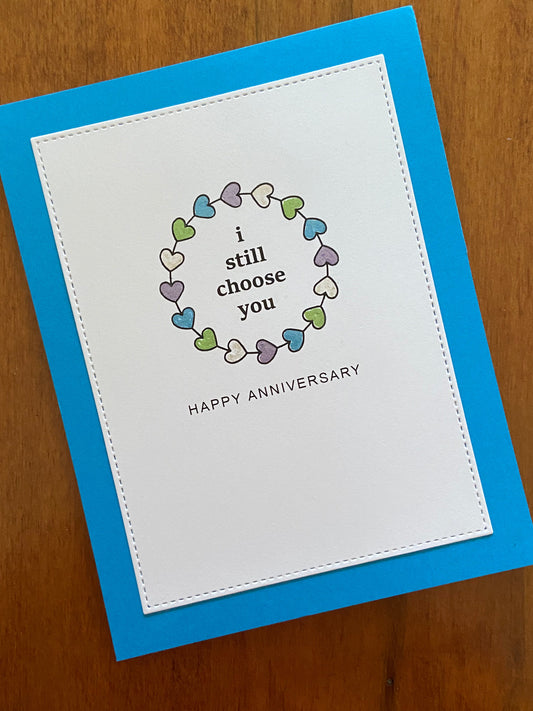 Anniversary card with heart wreath coloured in metalic gel pens and text 'i still choose you' on a white panel mounted to a blue notecard.