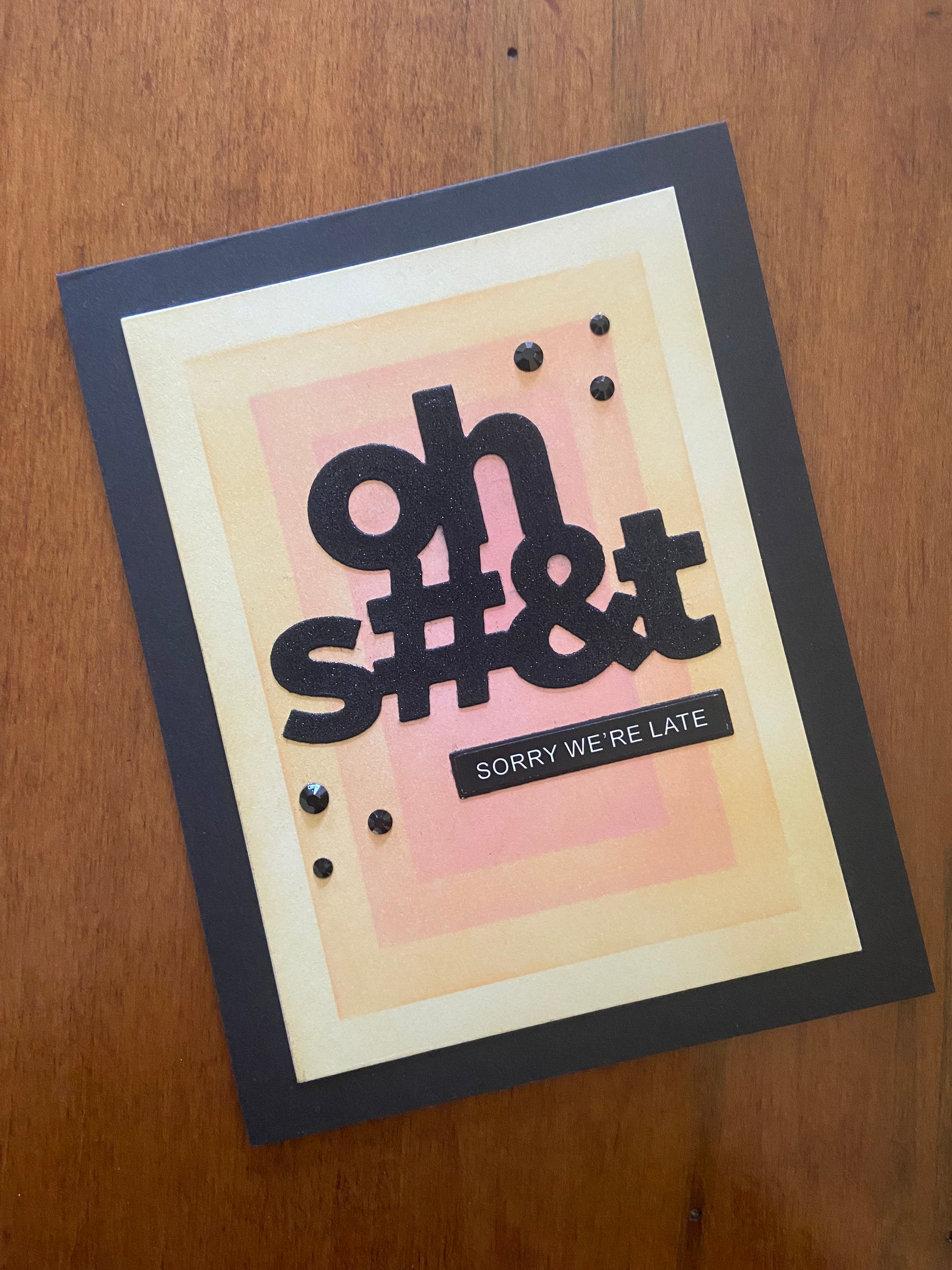 Black note card with a pink, orange, and yellow rectangular geometric ink blended pattern in the centre. There is a  bold black oh S#&T Sorry we're late sentiment.  