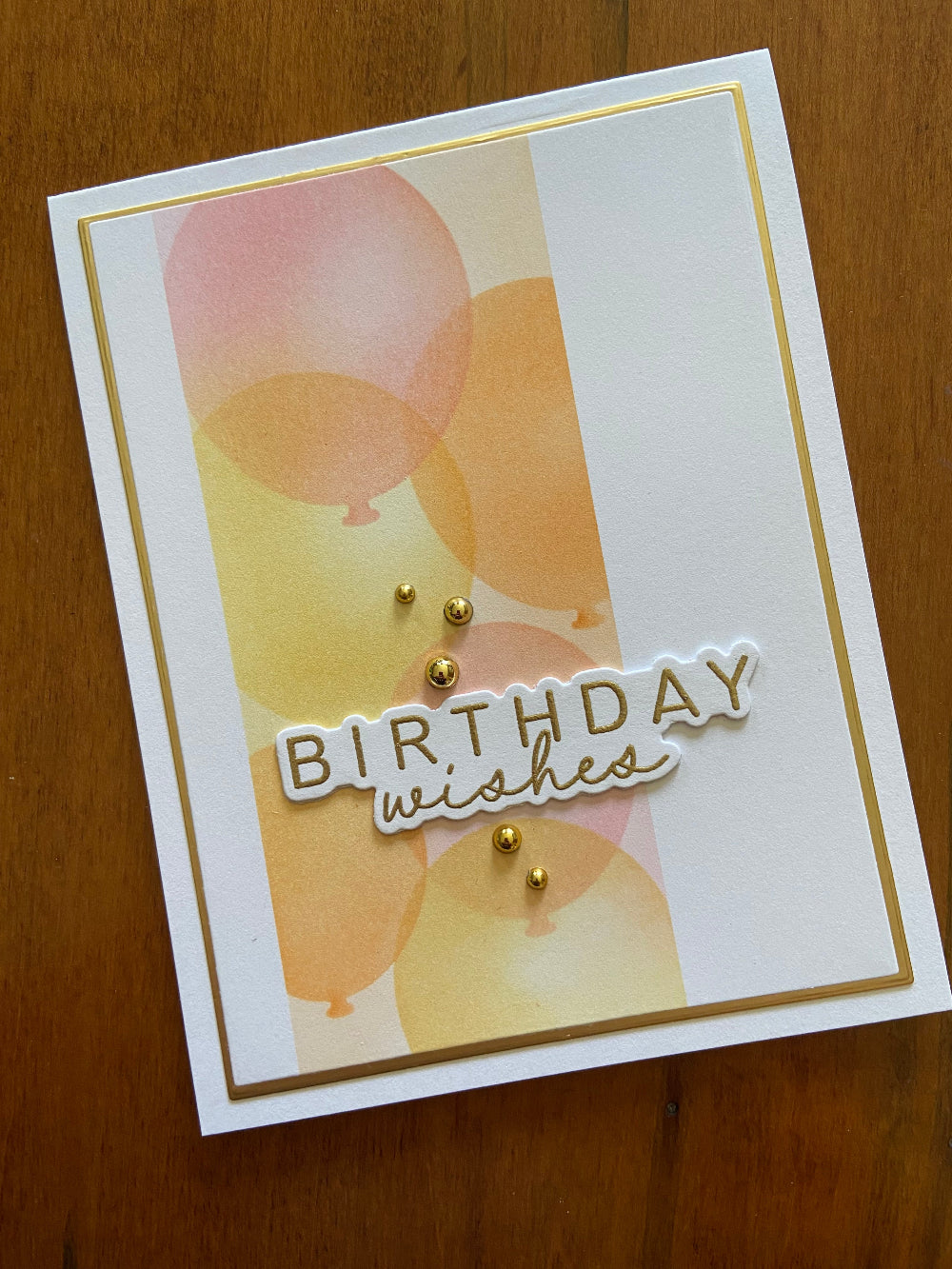 Handmade birthday card with stencilled pink, yellow and orange balloons with gold accents and 'Birthday Wishes' mixed font text.
