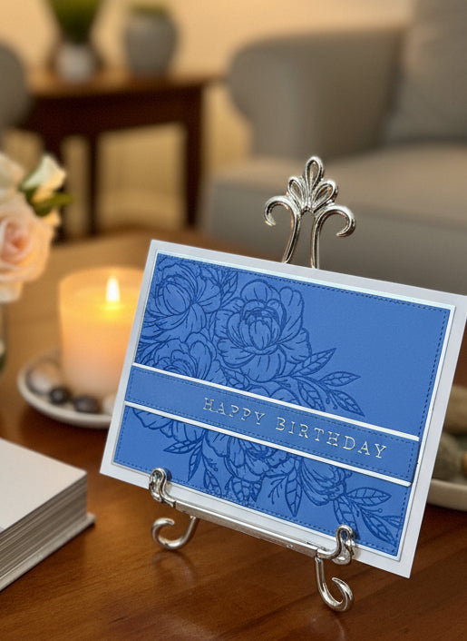 Blue birthday card with floral design with silver accents on a stand in a home setting
