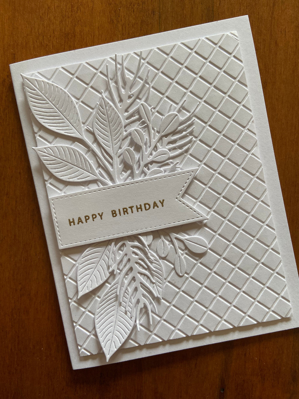 A sophisticated white on white handmade birthday card with embossed foliage design and the text 'Happy Birthday' heat embossed in gold.