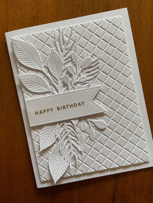 A sophisticated white on white handmade birthday card with embossed foliage design and the text 'Happy Birthday' heat embossed in gold.