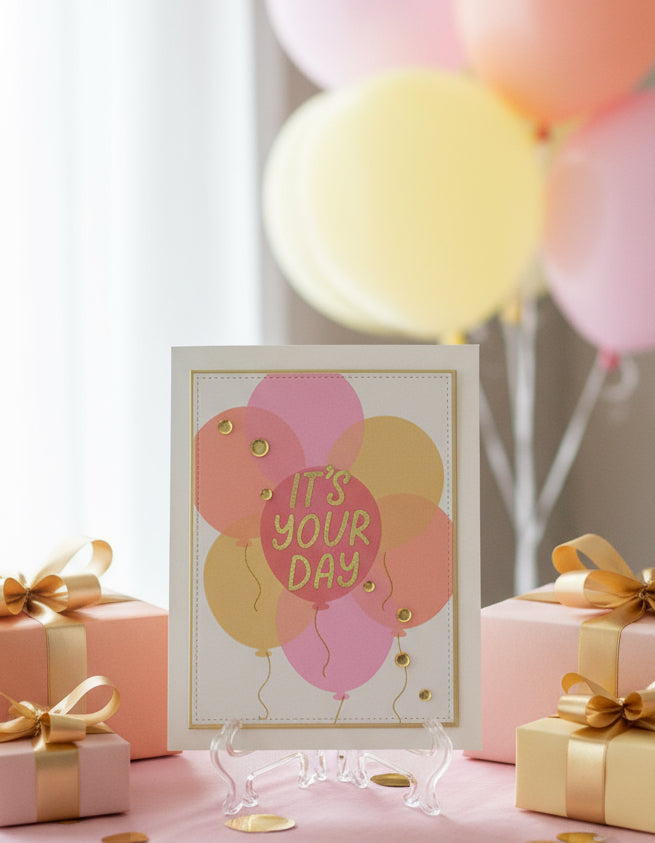 Card with 'It's Your Day' text and balloons, surrounded by gift boxes and balloons on a light background