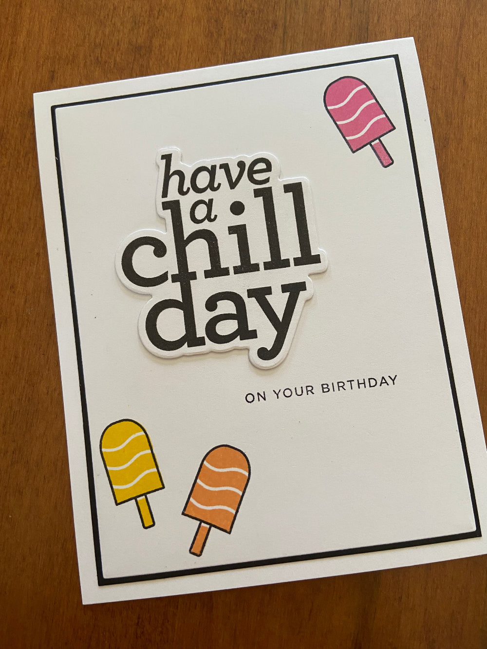 A handmade birthday card with stamped popsicles and the text 'have a chill day' on it, mounted on a white notecard with a black mat.
