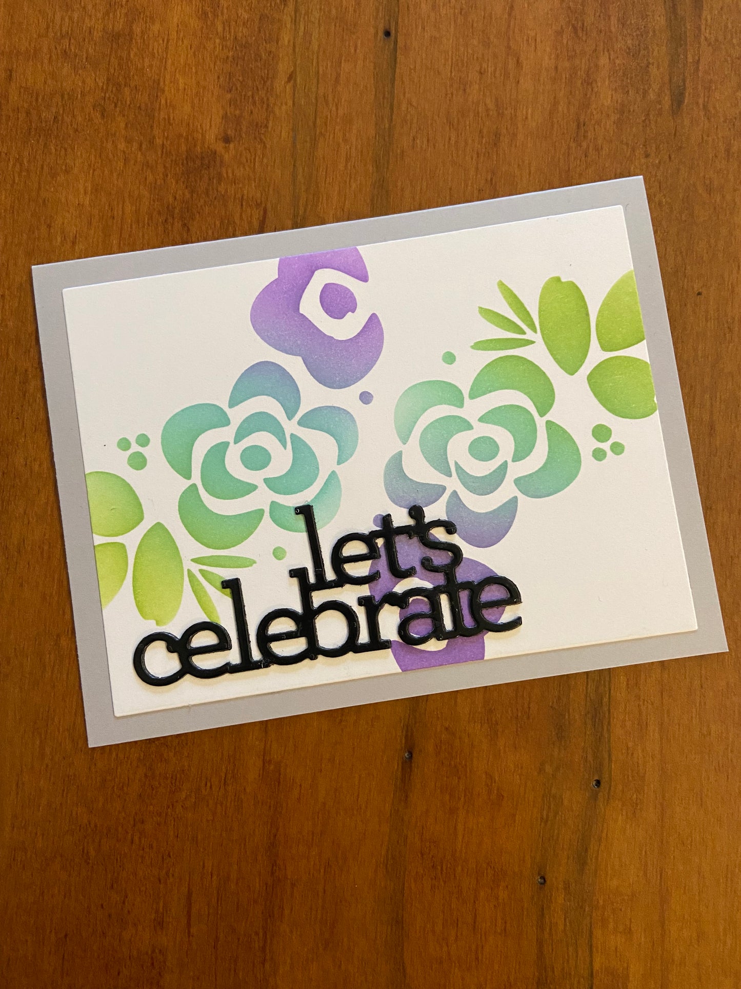 Handmade Let's Celebrate card with stencilled modern flowers in purple, blue and green with glossy black die-cut sentiment on white notecard - front view of 4.25x5.5 celebration card