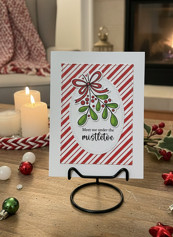 Christmas card with mistletoe design on a stand, surrounded by candles and decorations.