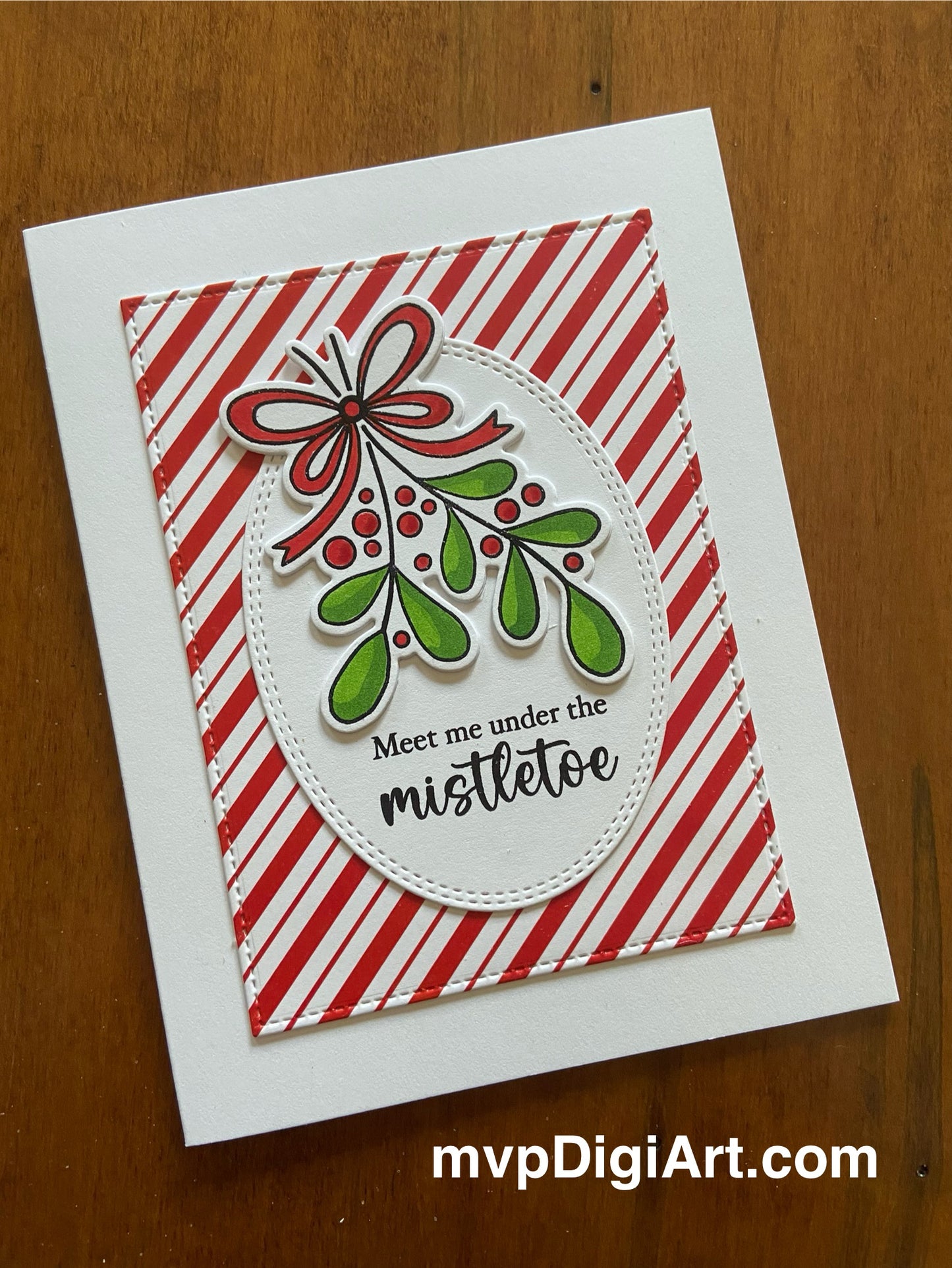 A handmade Christmas card with a hand-coloured image of mistletoe on white oval layered onto a red and white candy striped background, and the text 'Meet me under the mistletoe' stamped below.