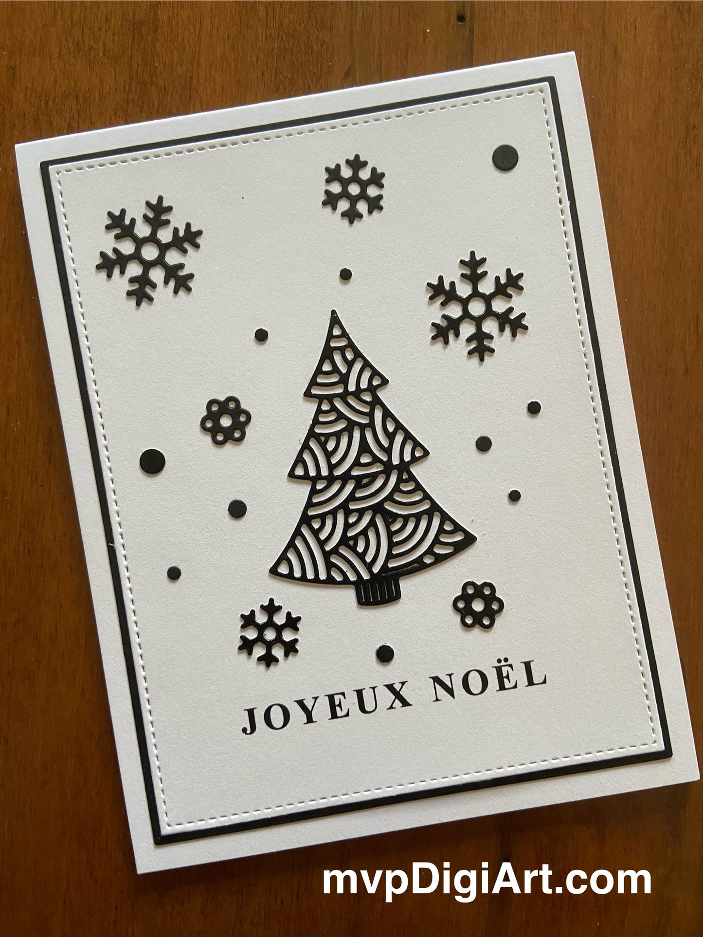 A handmade French Christmas card featuring a black ornate tree and snowflakes with the phrase 'Joyeux Noël' on a white background, mounted on a black cardstock mat.