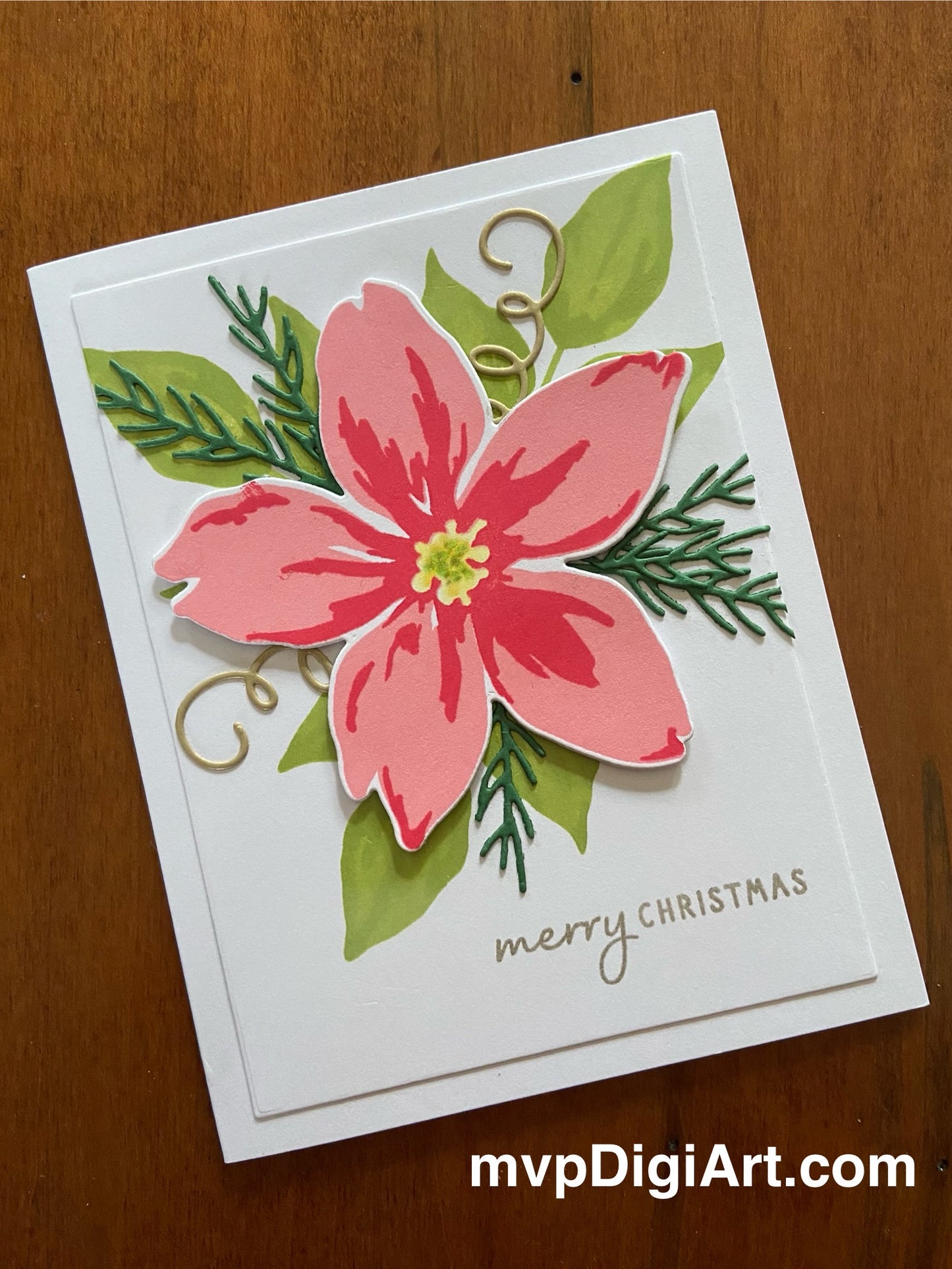 Handmade Christmas card with a pink poinsettia flower with greenery and spruce sprigs on white background with gold 'Merry Christmas' text in mixed fonts.