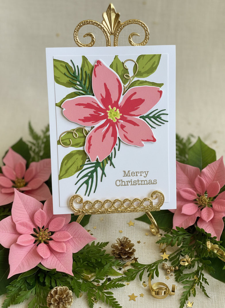 Handmade Christmas card with a pink poinsettia flower with greenery and spruce sprigs on white background with gold 'Merry Christmas' text in a single font on a decorated table
