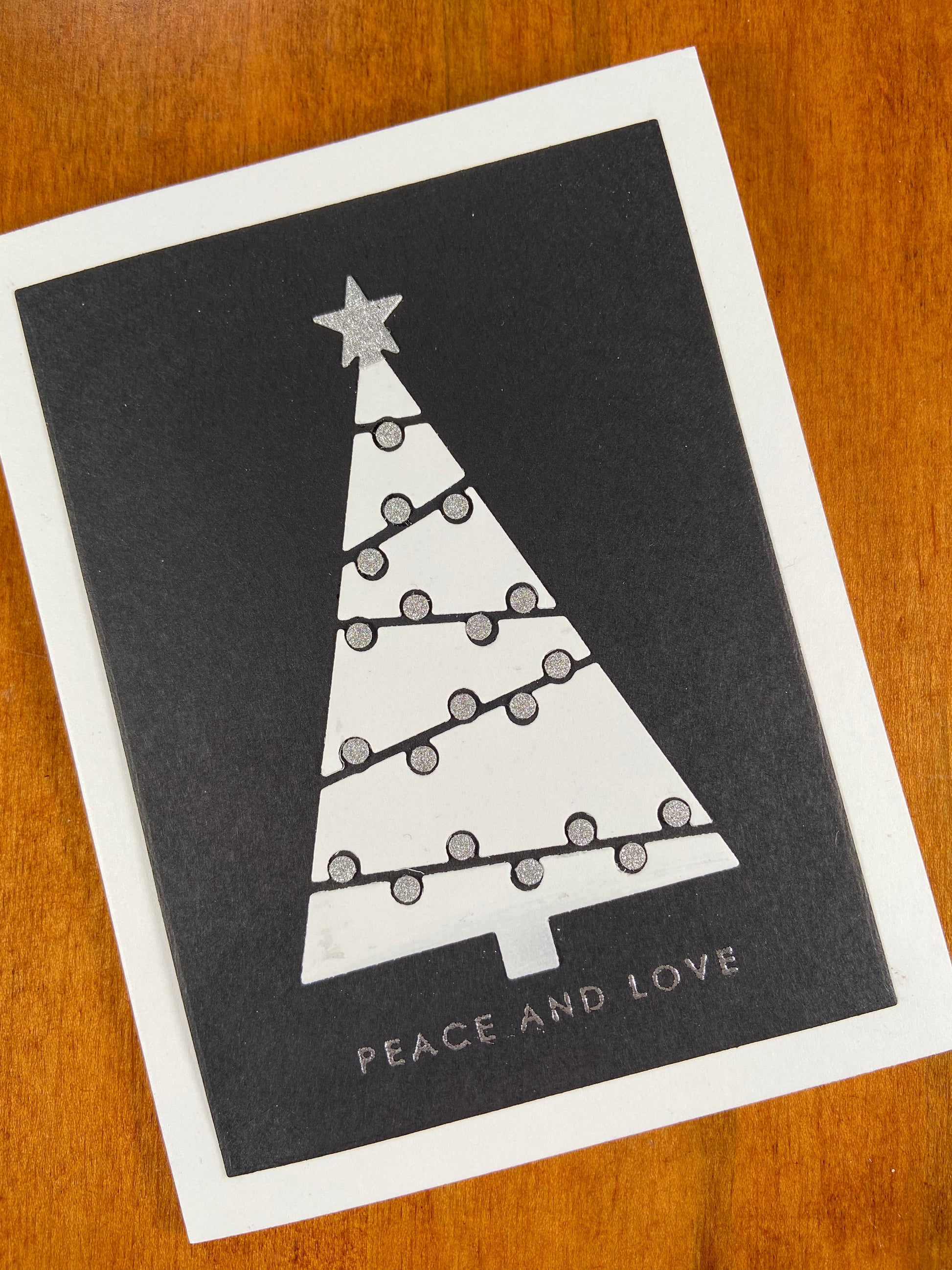 Handmade Christmas card with modern graphic Christmas tree in black, white, and silver monochrome design, silver text ‘peace and joy’