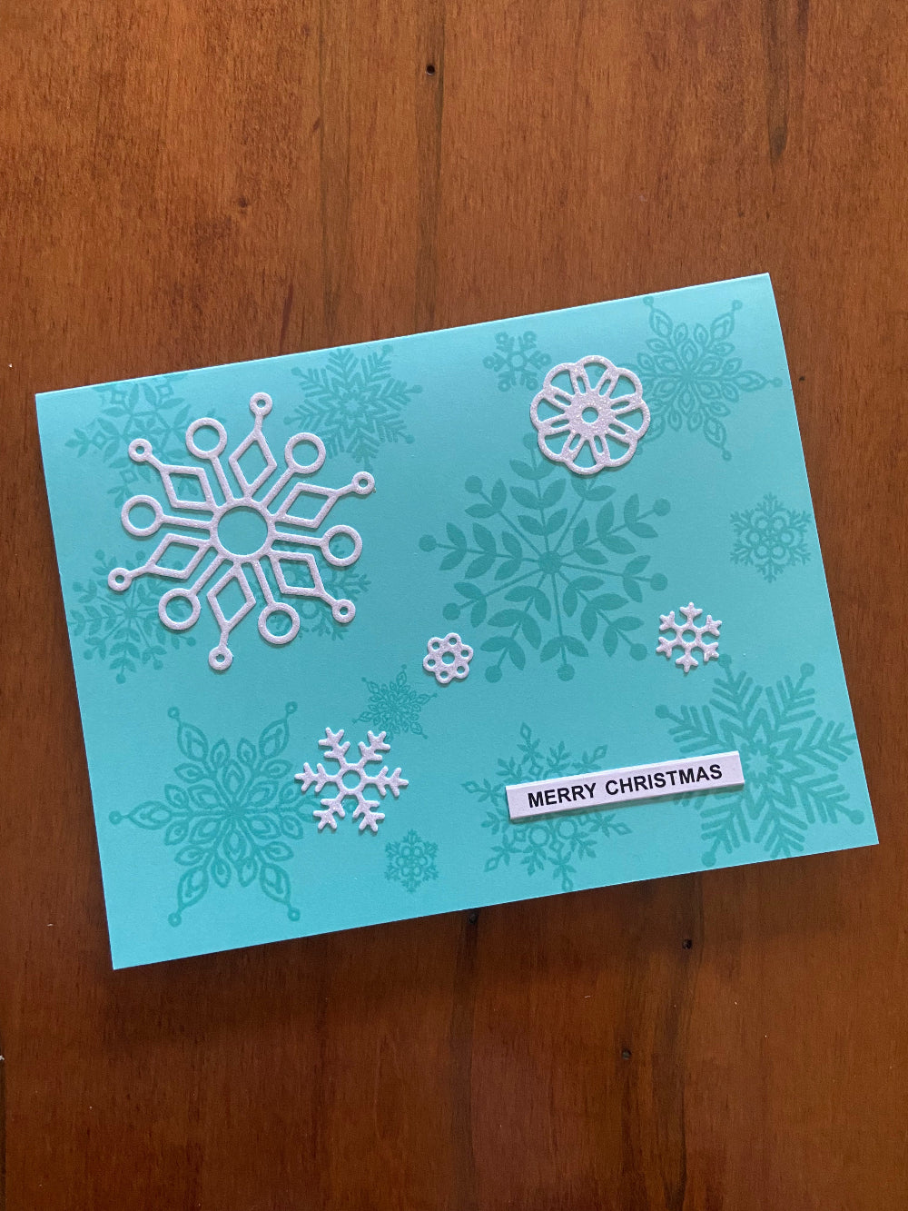 Turquoise Christmas card with turquoise and whte snowflakes and 'Merry Christmas' text 