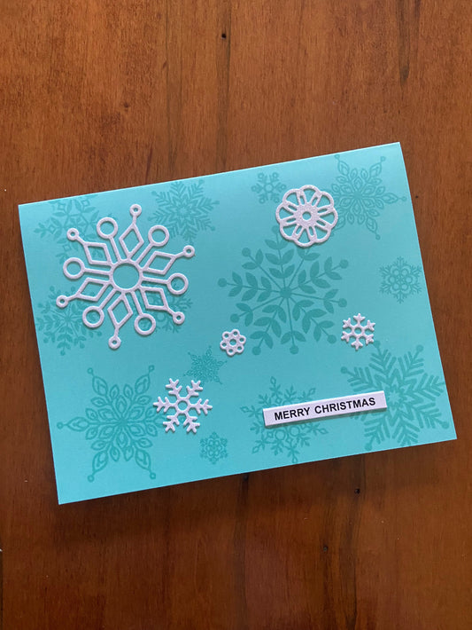 Turquoise Christmas card with turquoise and whte snowflakes and 'Merry Christmas' text 