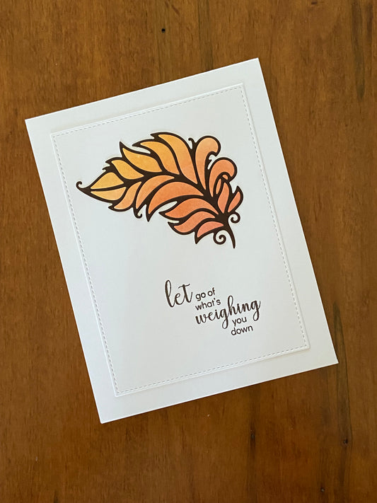 Let go of what’s weighing you down encouragement handmade card. An ink blend in pink, orange, and yellow are inlaid in a feather die cut that is the focal point of the card in chocolate brown. 