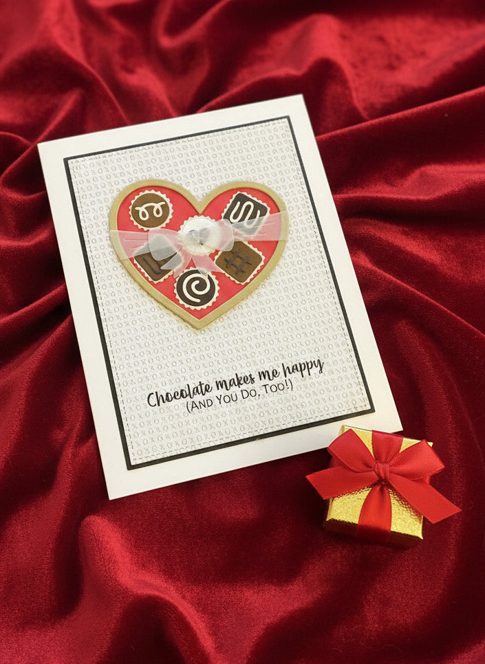 Card with heart-shaped chocolate design and small gift box on red fabric