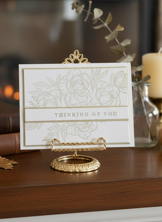 Floral gold outline 'Thinking of You' card on a decorative stand with candle and greenery decorations