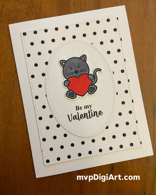 A hand-crafted Valentine's Day card featuring a grey cat holding a red heart with the text 'Be my Valentine' on a white oval, with a black and white Swiss dot background.