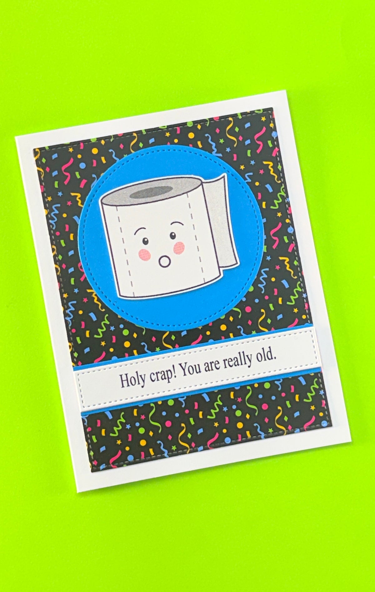 Handmade birthday card using black Confetti Background patterned cardstock, featuring a cartoon toilet roll on a blue circle and the sentiment ‘Holy crap! You are really old.’