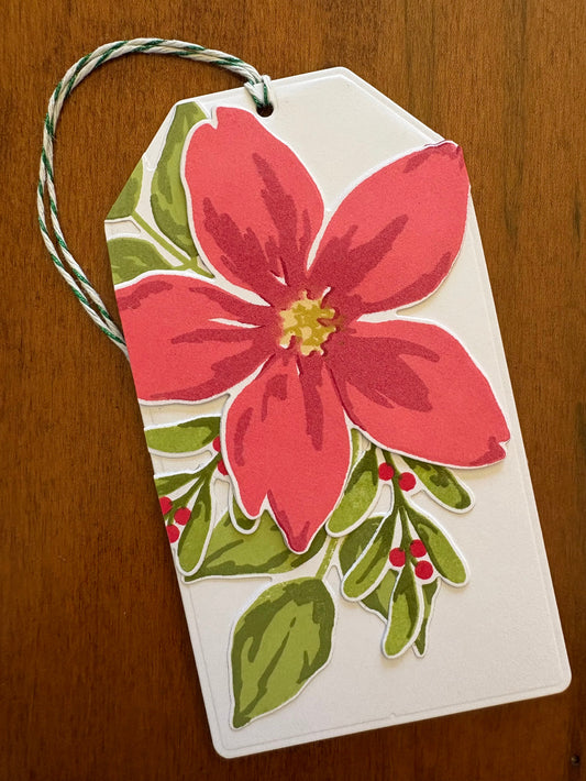 White gift card holder tag with a large red poinsettia bloom, greenery and red berries.