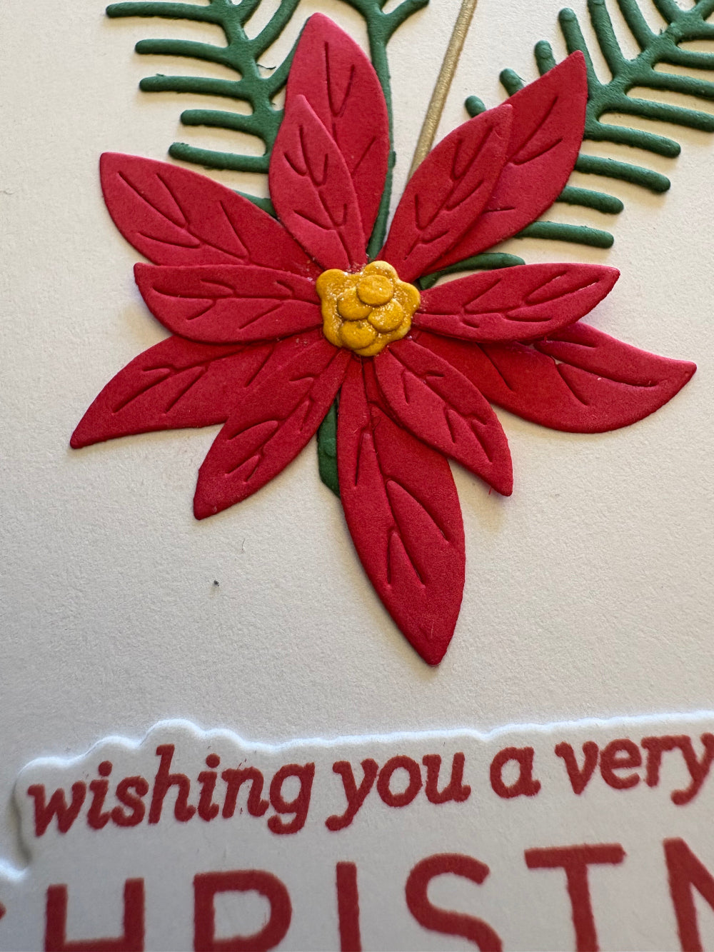 Close up of red poinsettia flower and green pine sprigs on a Christmas gift card holder tag.