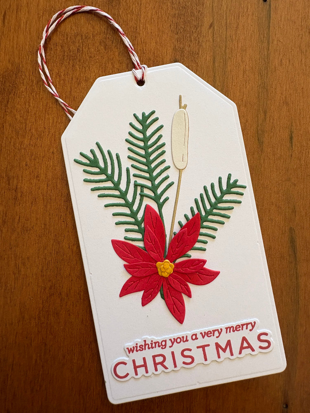White Christmas gift card holder tag with poinsettia, pine sprigs and a cat tail, text 'wishing you a very merry Christmas'