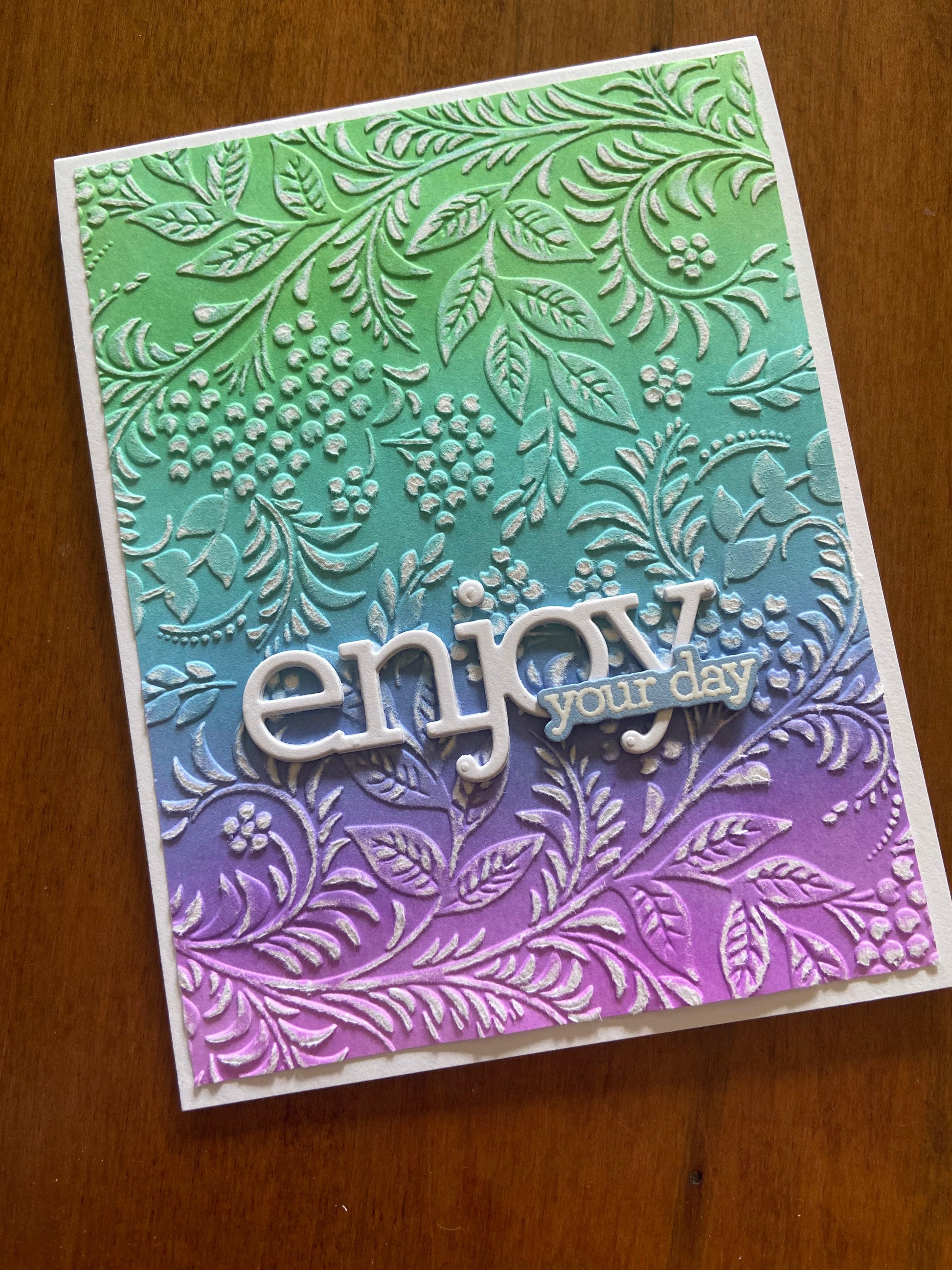 Colorful card with floral embossed pattern ink blended in shades of purple to green with and 'enjoy your day' text die cut