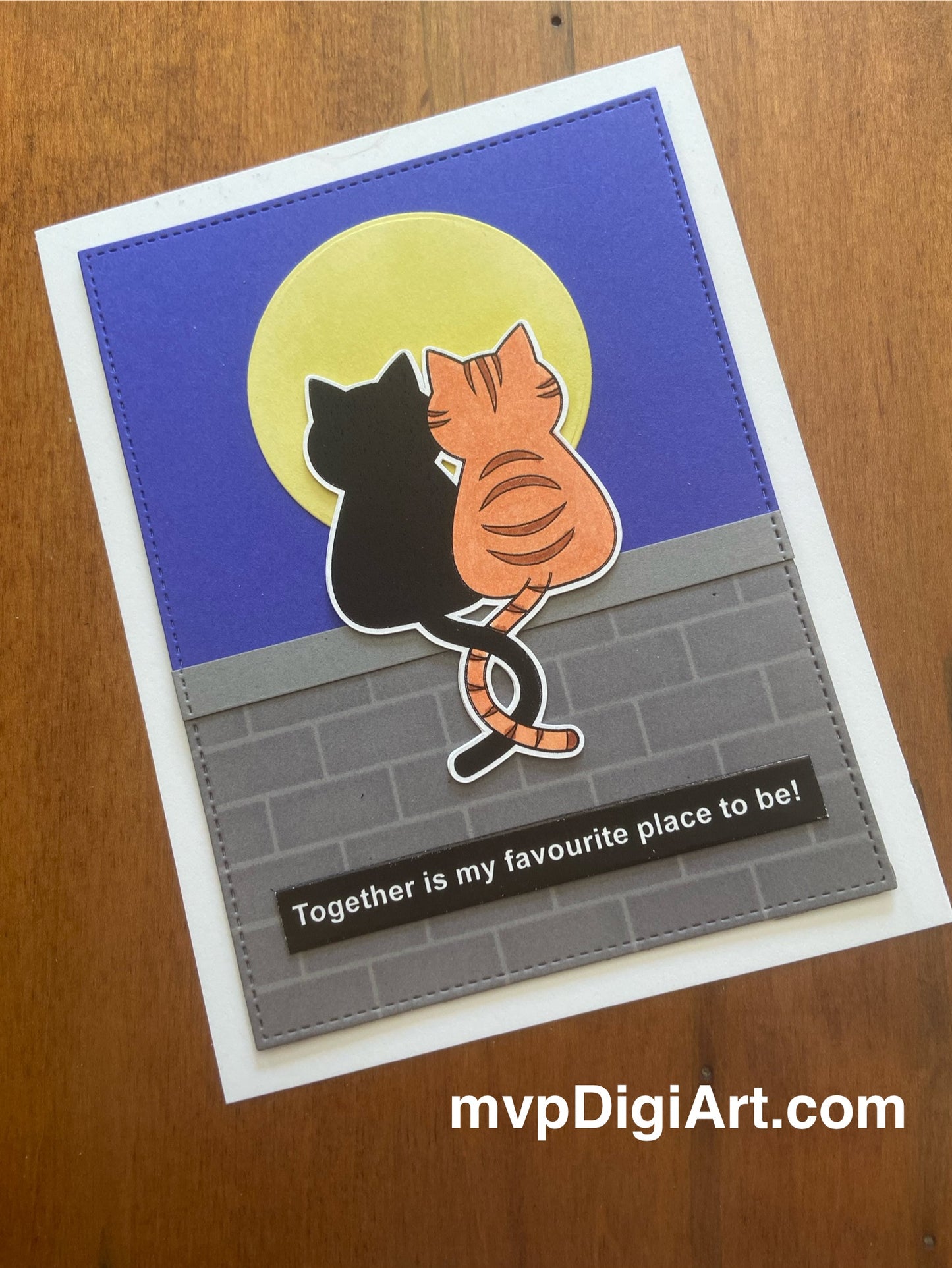 Card with two cats with tails entwined sitting on wall under the moon. White text on black 'together is my favourite place to be'
