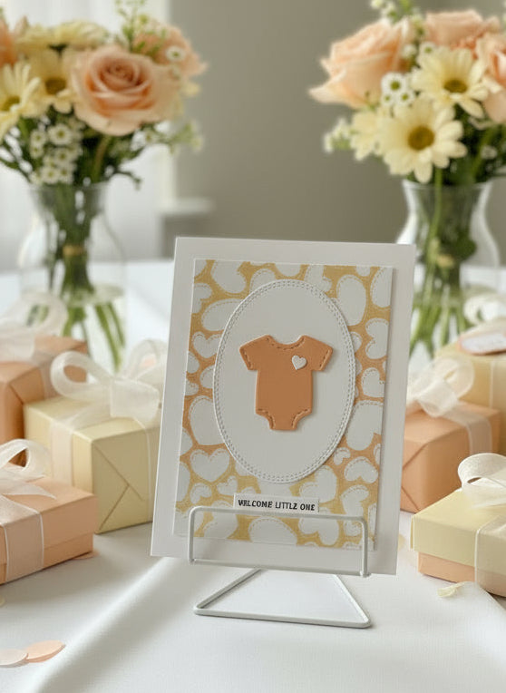 Baby shower card with orange baby onesie on a floral background, surrounded by gift boxes and balloons.