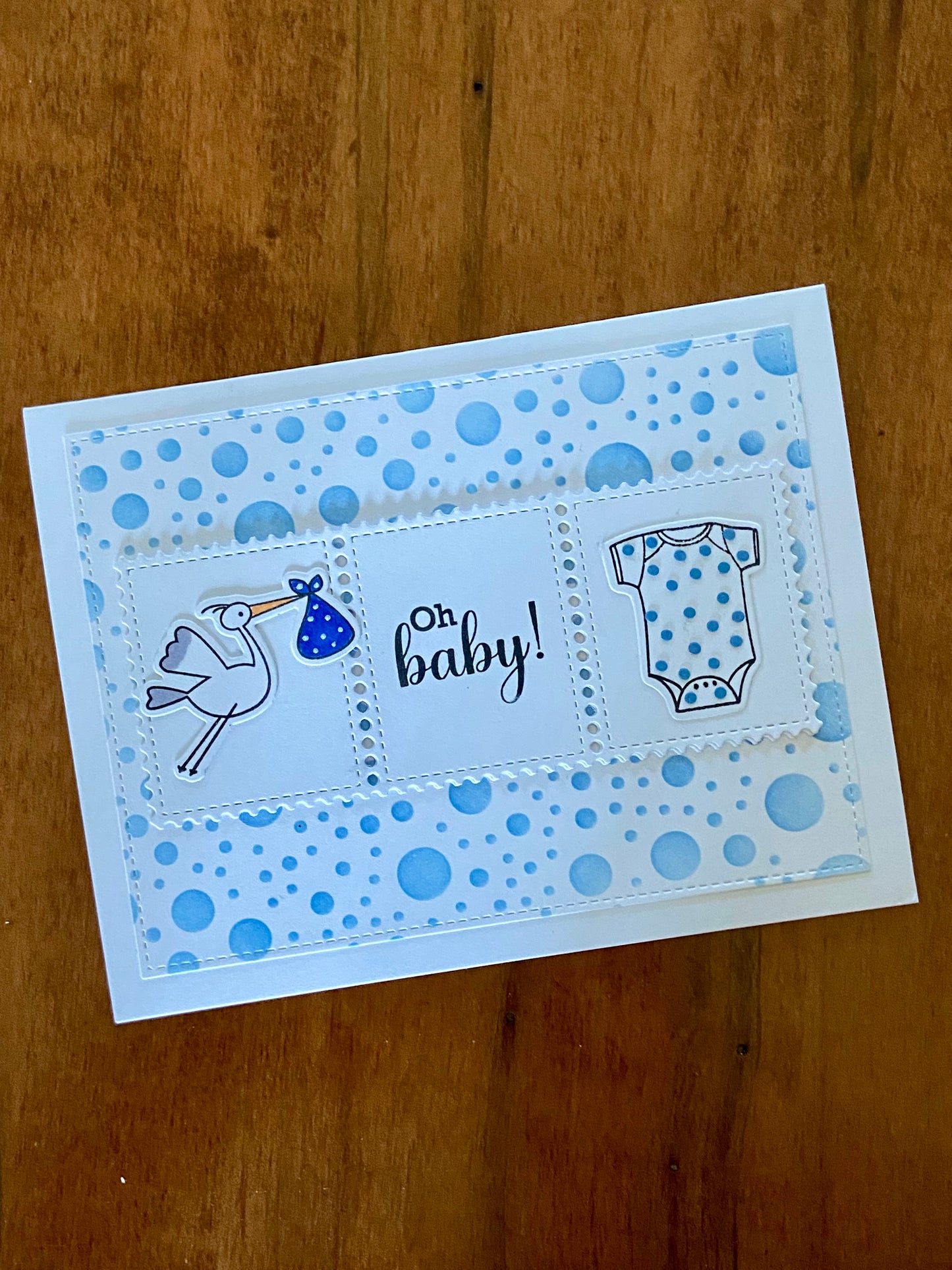 Oh Baby Shower card. Blue polka dot background. A rectangular centre panel with a stork carrying a blue bundle and white onsie with tiny blue dots and the sentiment Oh Baby in between. 