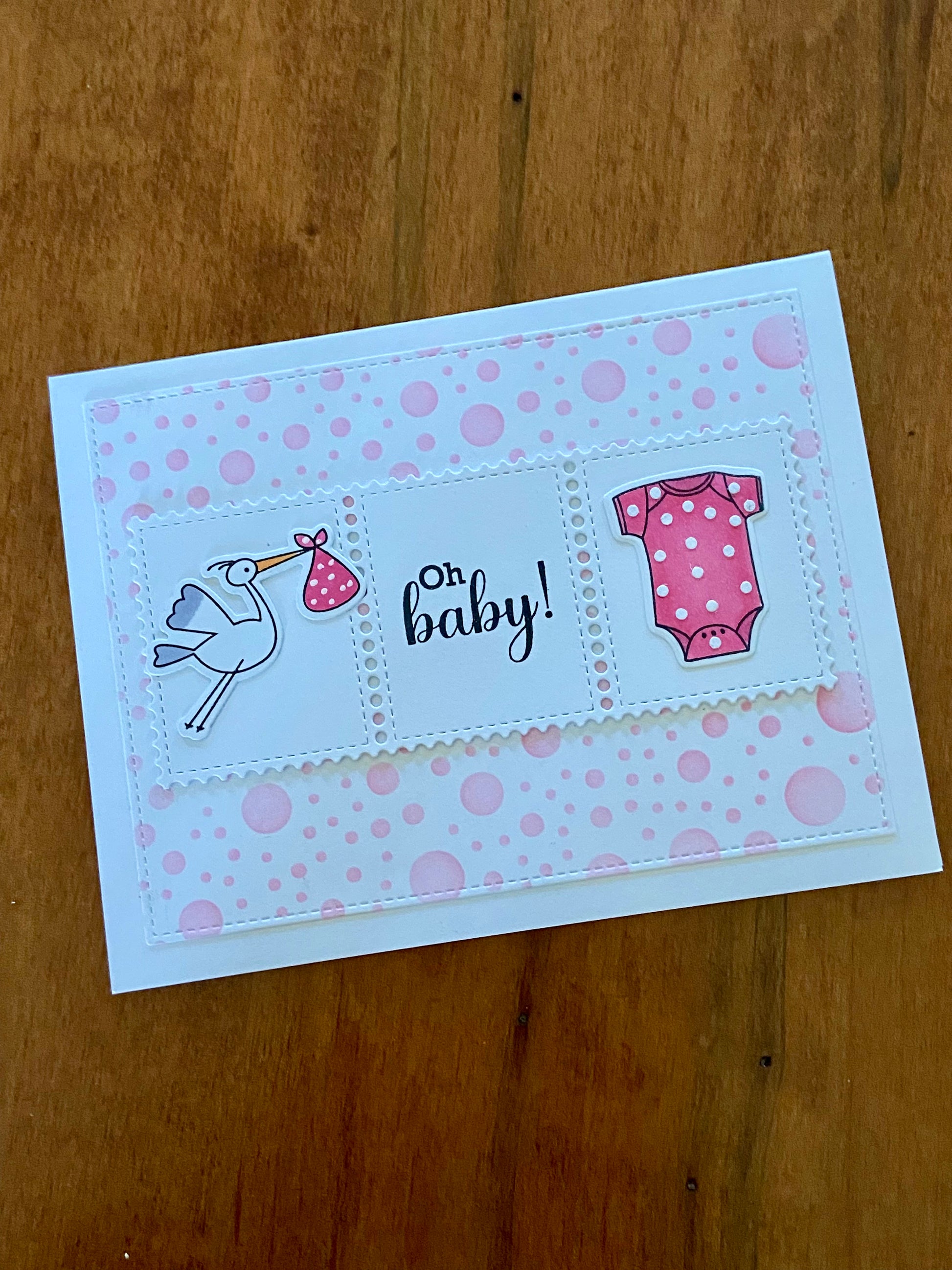 Oh Baby Shower card. Pink polka dot background. A rectangular centre panel with a stork carrying a pink bundle and pink onsie with tiny white dots and the sentiment Oh Baby in between. 